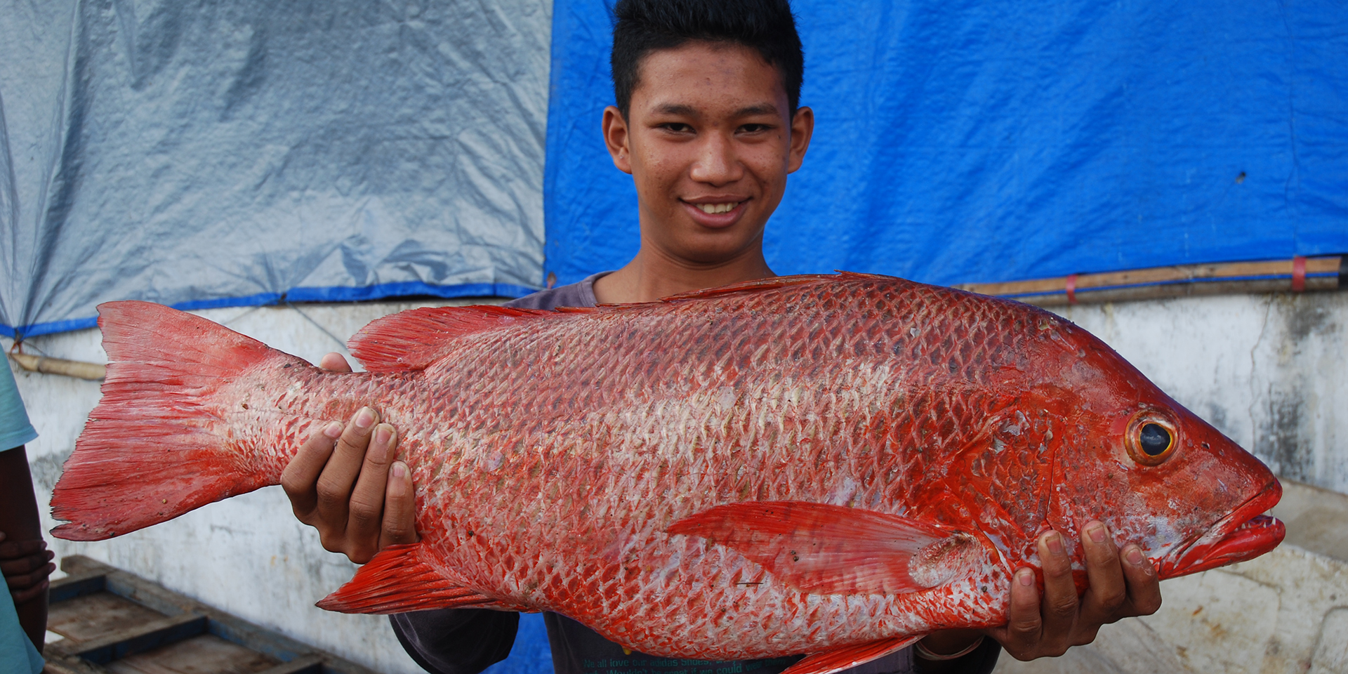 Image of a young man smiling and presenting a large red fish