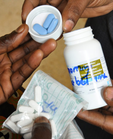 Image of a person giving medication to people in the form of pills.