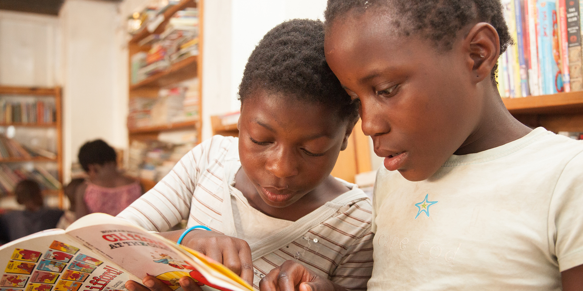 Two young girls reading a book together.