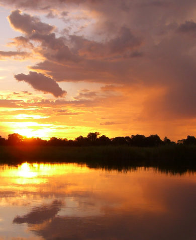 Image of the sun setting on a large lake with a forest on the horizon.
