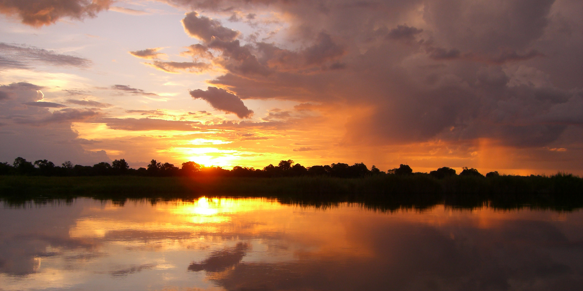 Image of the sun setting on a large lake with a forest on the horizon.