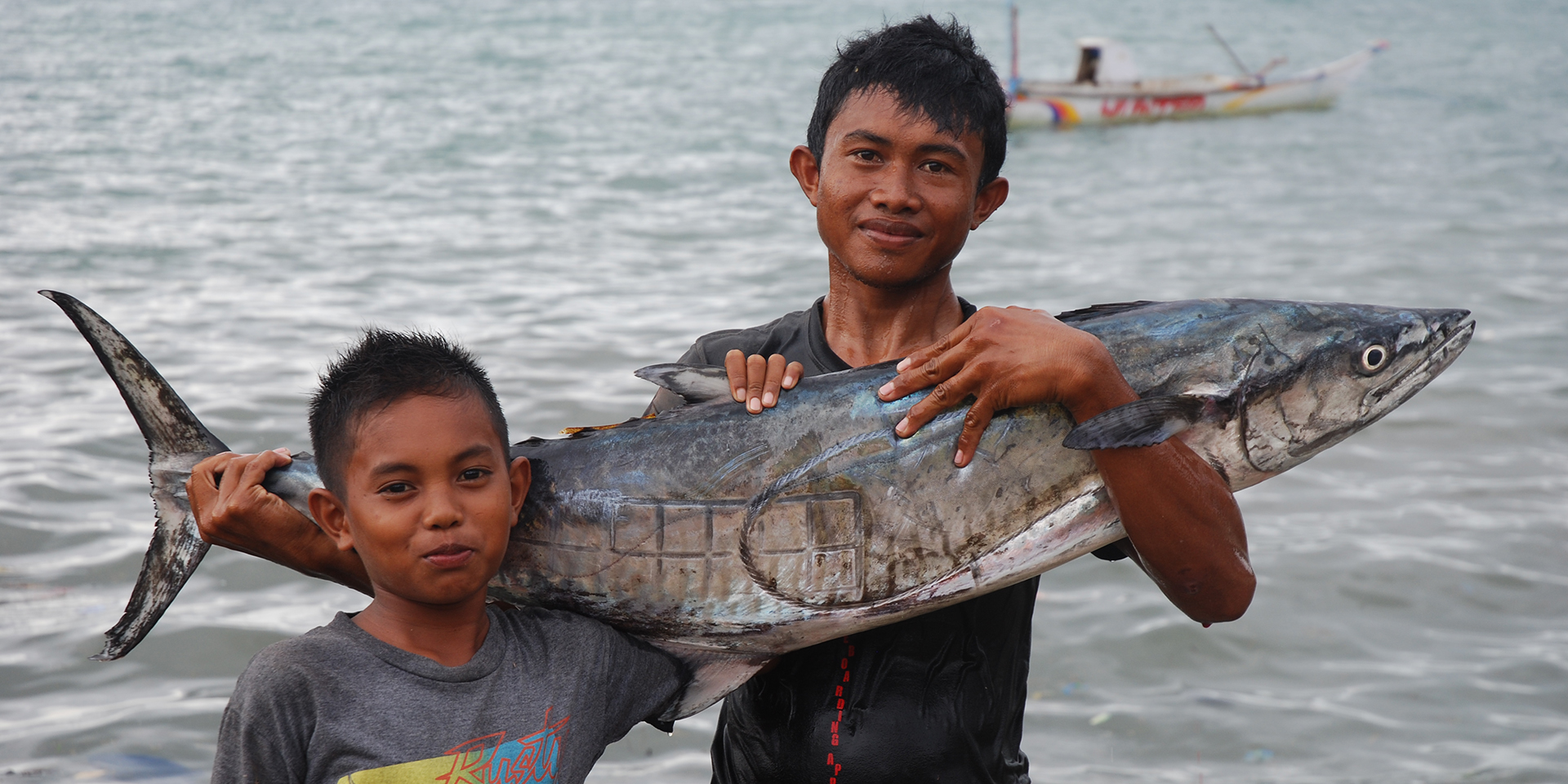 Image of a man and young boy holding up a large fish and smiling.
