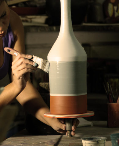 A woman painting a piece of pottery that is spinning on a pottery wheel.