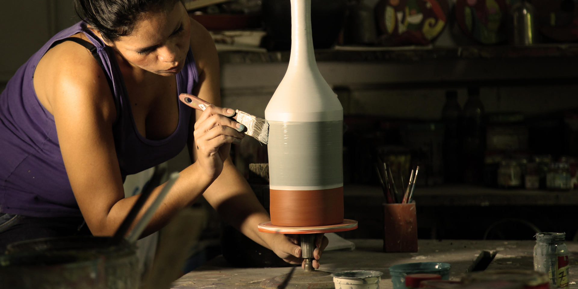 A woman painting a piece of pottery that is spinning on a pottery wheel.