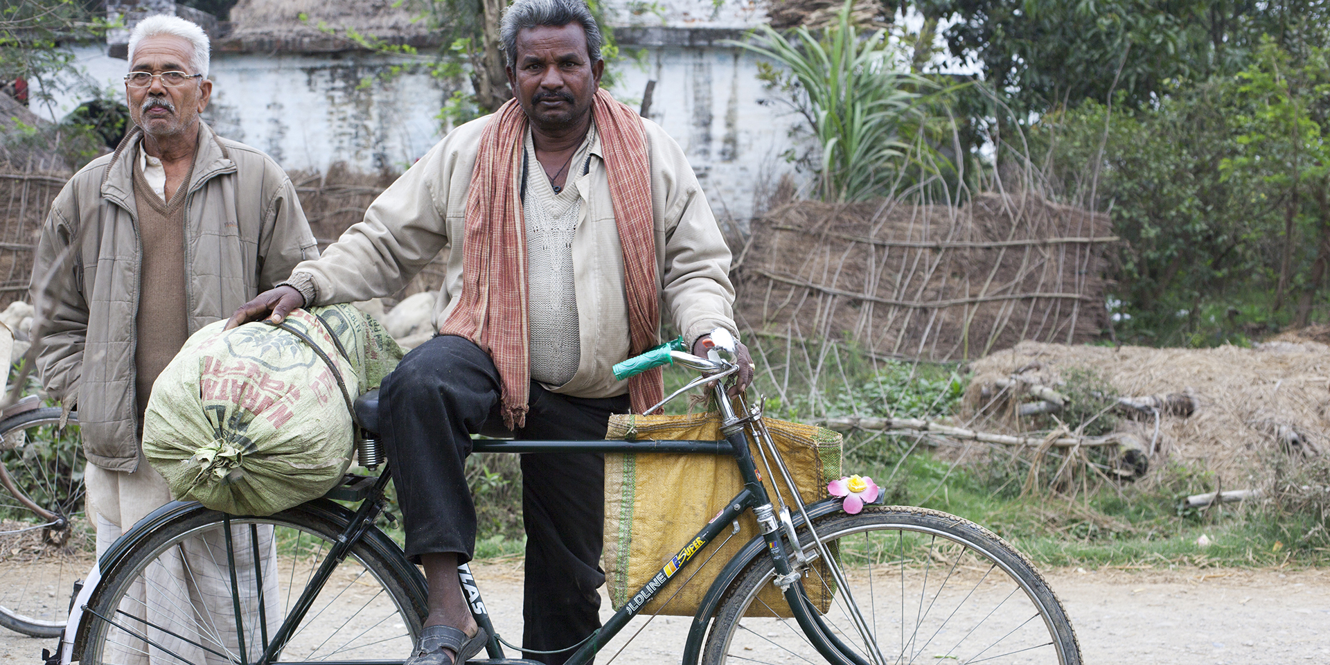 A man posing on a bicycle on a road with a village in the background.