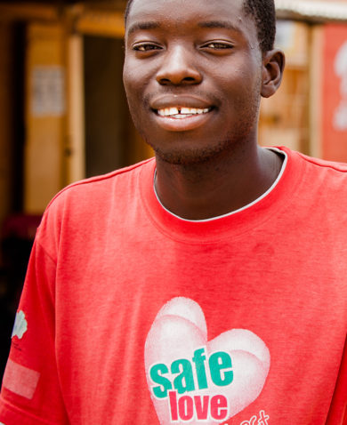 Image of a smiling young man on a busy street wearing a red t-shirt that says "Safe Love."