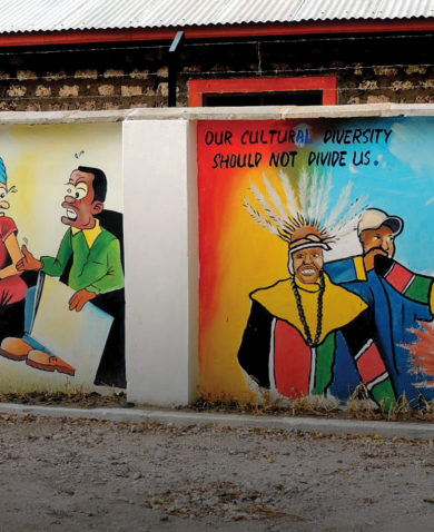 Image of two brightly colored murals side by side on a dividing wall. One addresses conflict resolution while the other celebrates cultural diversity.