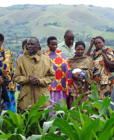 A large group of farmers standing in a field with a lush, mountainous landscape in the background.