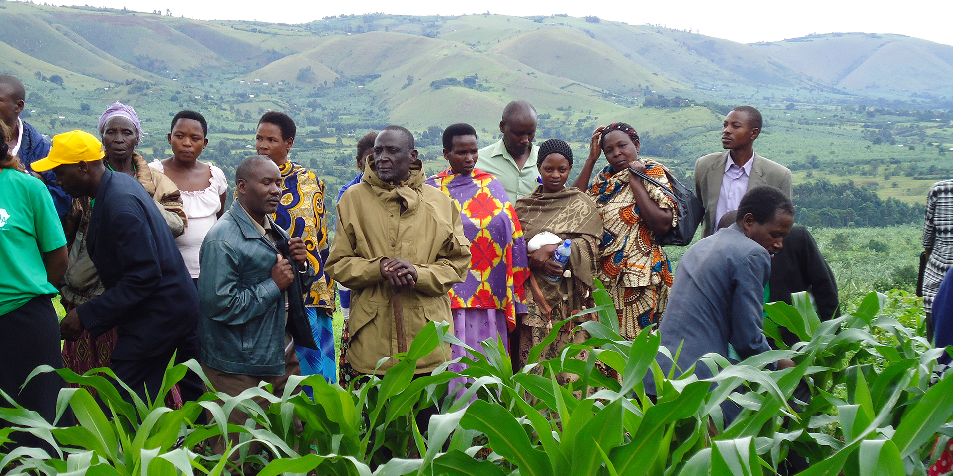 A large group of farmers standing in a field with a lush, mountainous landscape in the background.