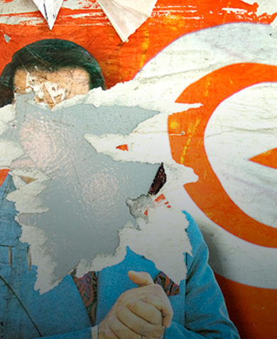A defaced political mural showing the face of a politician ripped down and the Tunisian flag in the background.