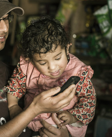 A man holding a small child and holding a cell phone up to her face so she can speak to someone.