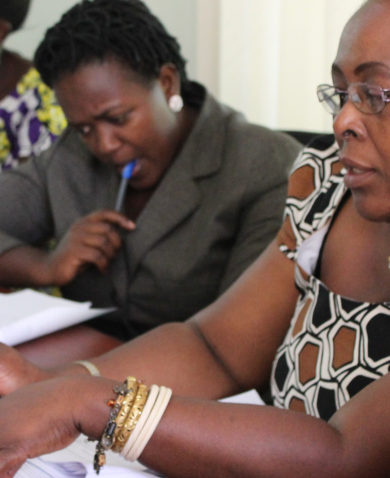 Image of women sitting at a conference table and discussing a hand-written document that partly reads "To strengthen the voice of PL HIV/AIDS in the country."