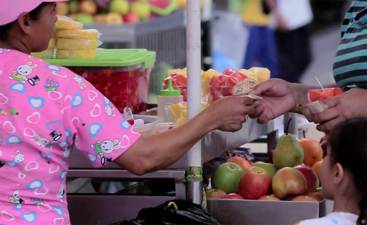 A fruit vendor accepting cash from a woman for a fruit bowl.