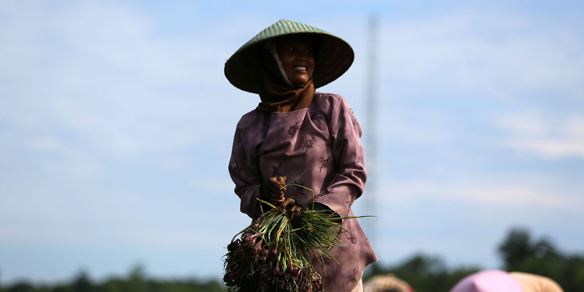Image of a smiling farmer holding a large bushel of crops in her hands.
