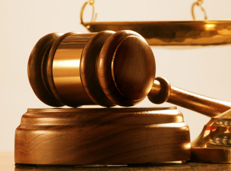 Image of a judge's gavel sitting beside a gold-plated scale.
