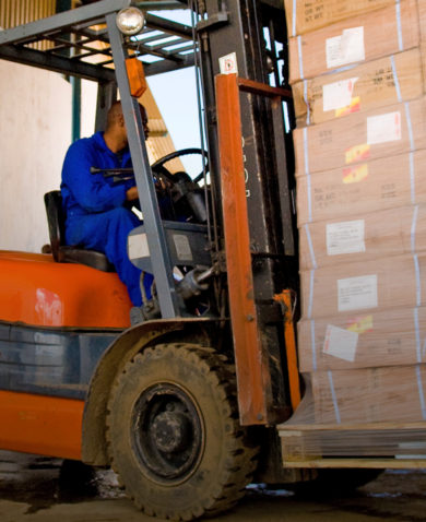Image of a worker driving a forklift carrying several palleted boxes.