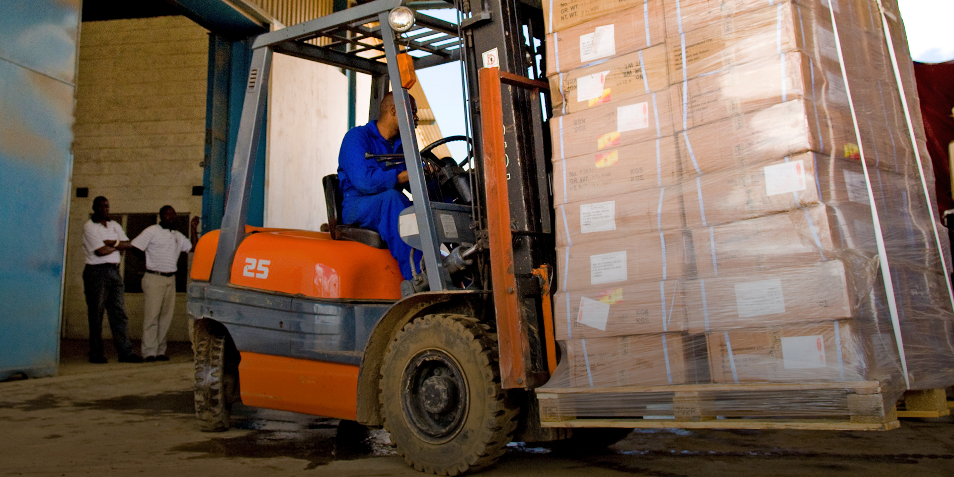 Image of a worker driving a forklift carrying several palleted boxes.