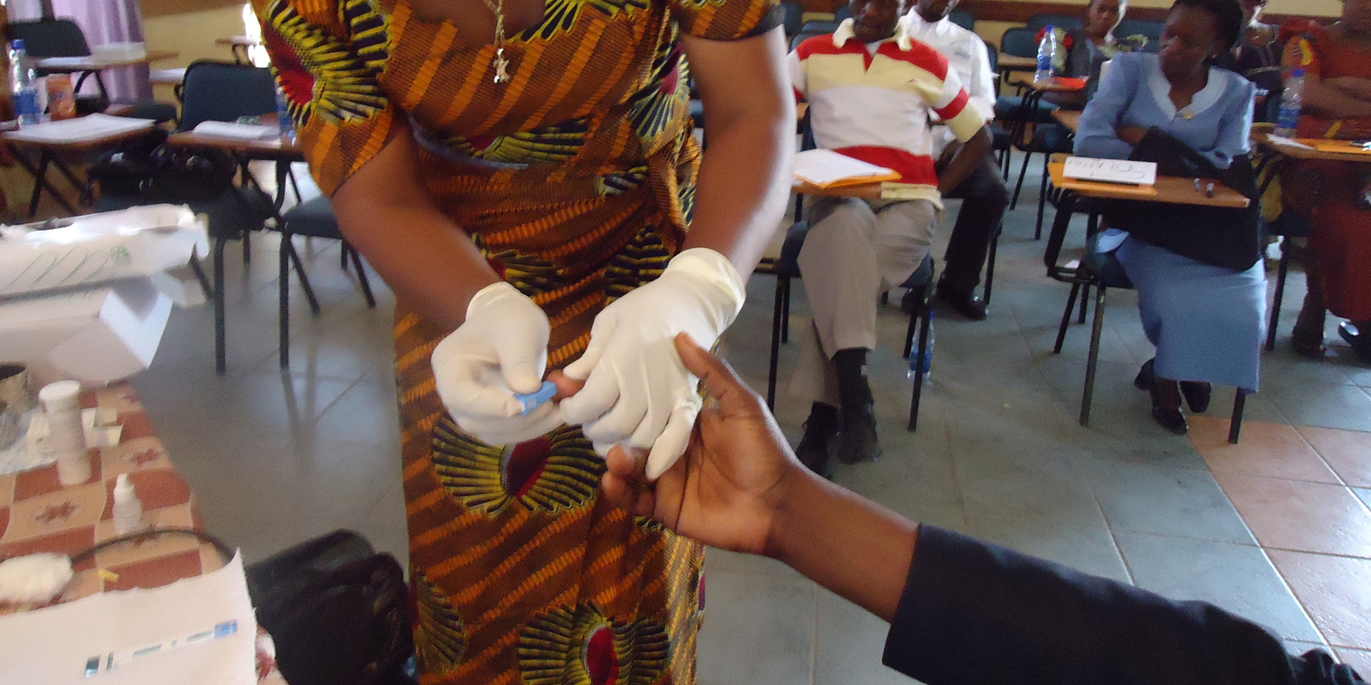 Image of a woman performing a medical test by pricking someone's finger.