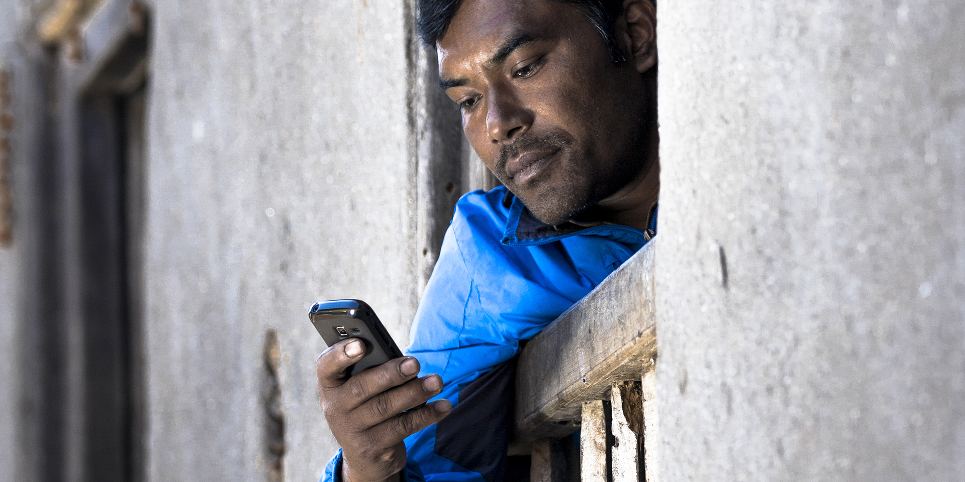 Image of a man leaning over the side of a balcony guard while looking at his cell phone.