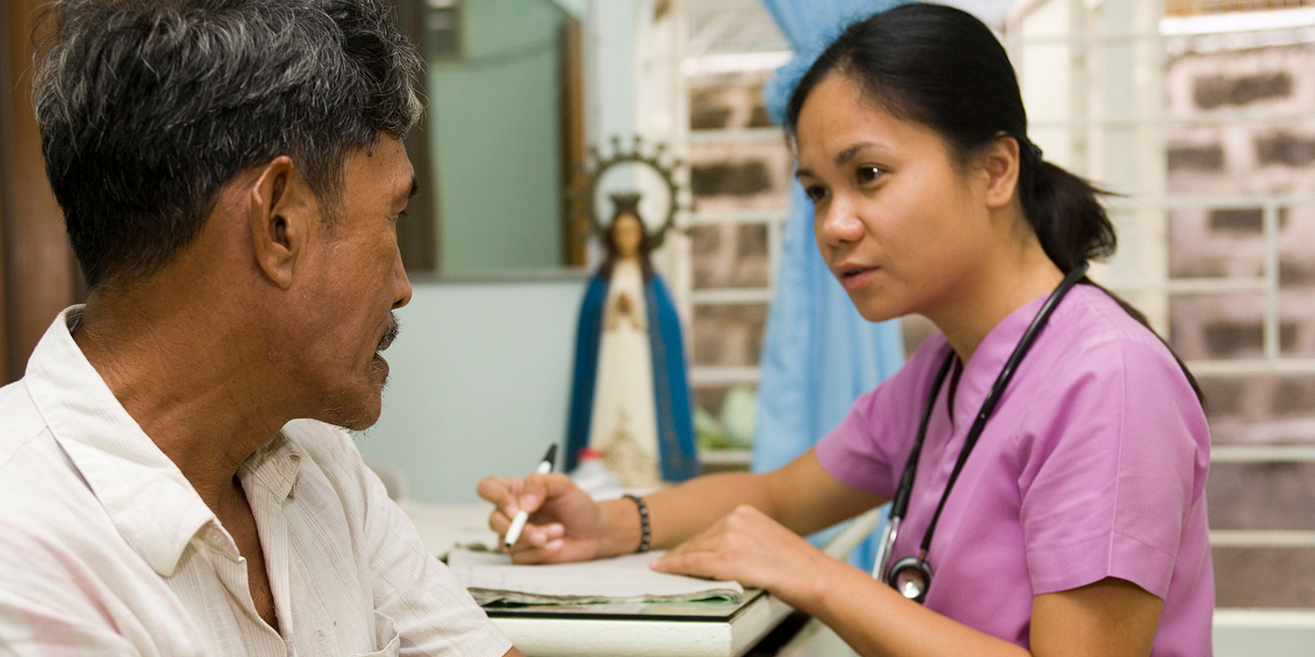 A healthcare worker interviewing a patient and taking notes.