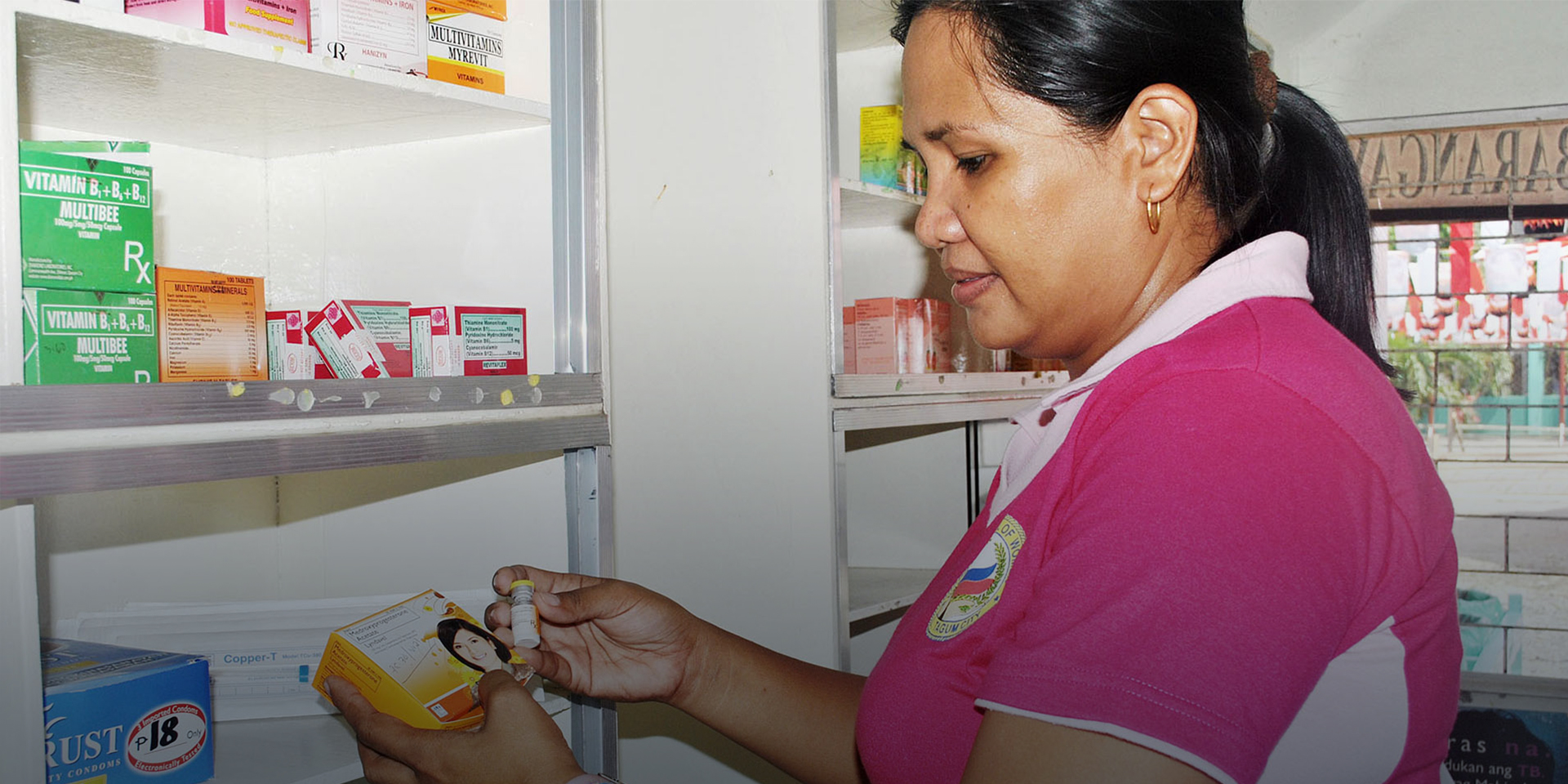 A woman holding and looking at a box of medication in a pharmacy.