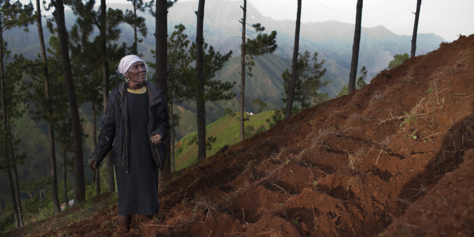 Image of a woman looking up a hill with freshly tilled red soil.