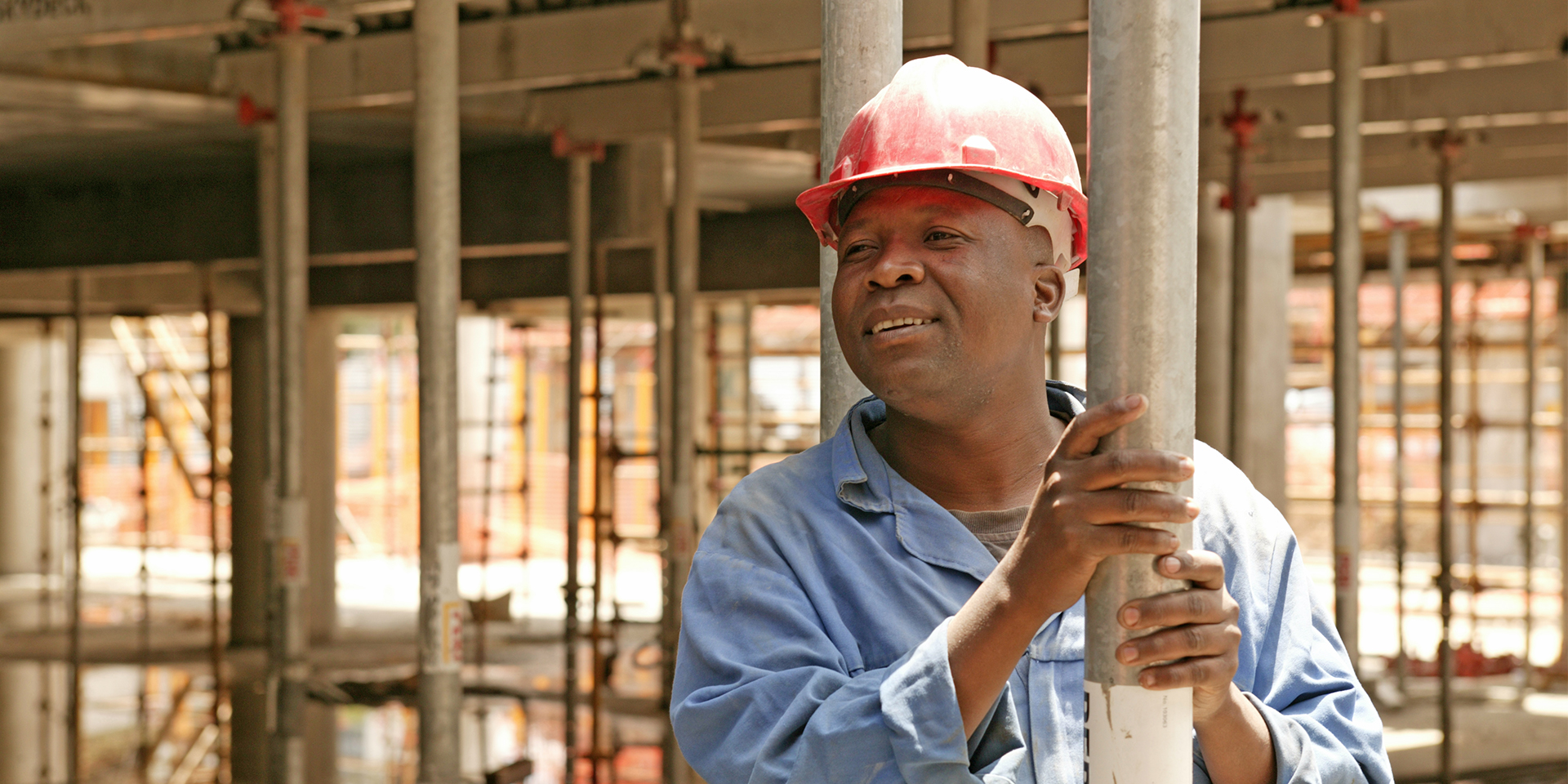 Image of a construction worker within a building under construction smiling and holding onto a steel girder.