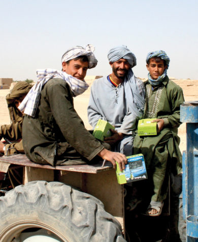 Image of several men smiling and sitting on a tractor with boxes in their hands.