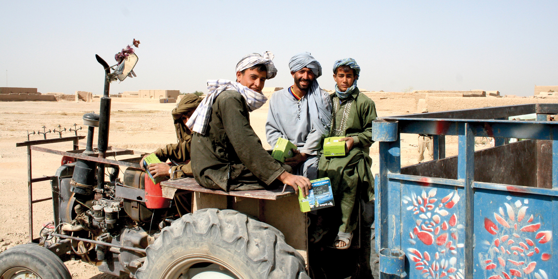 Image of several men smiling and sitting on a tractor with boxes in their hands.