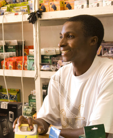 A man smiling and selling a cell phone to a customer in a store.