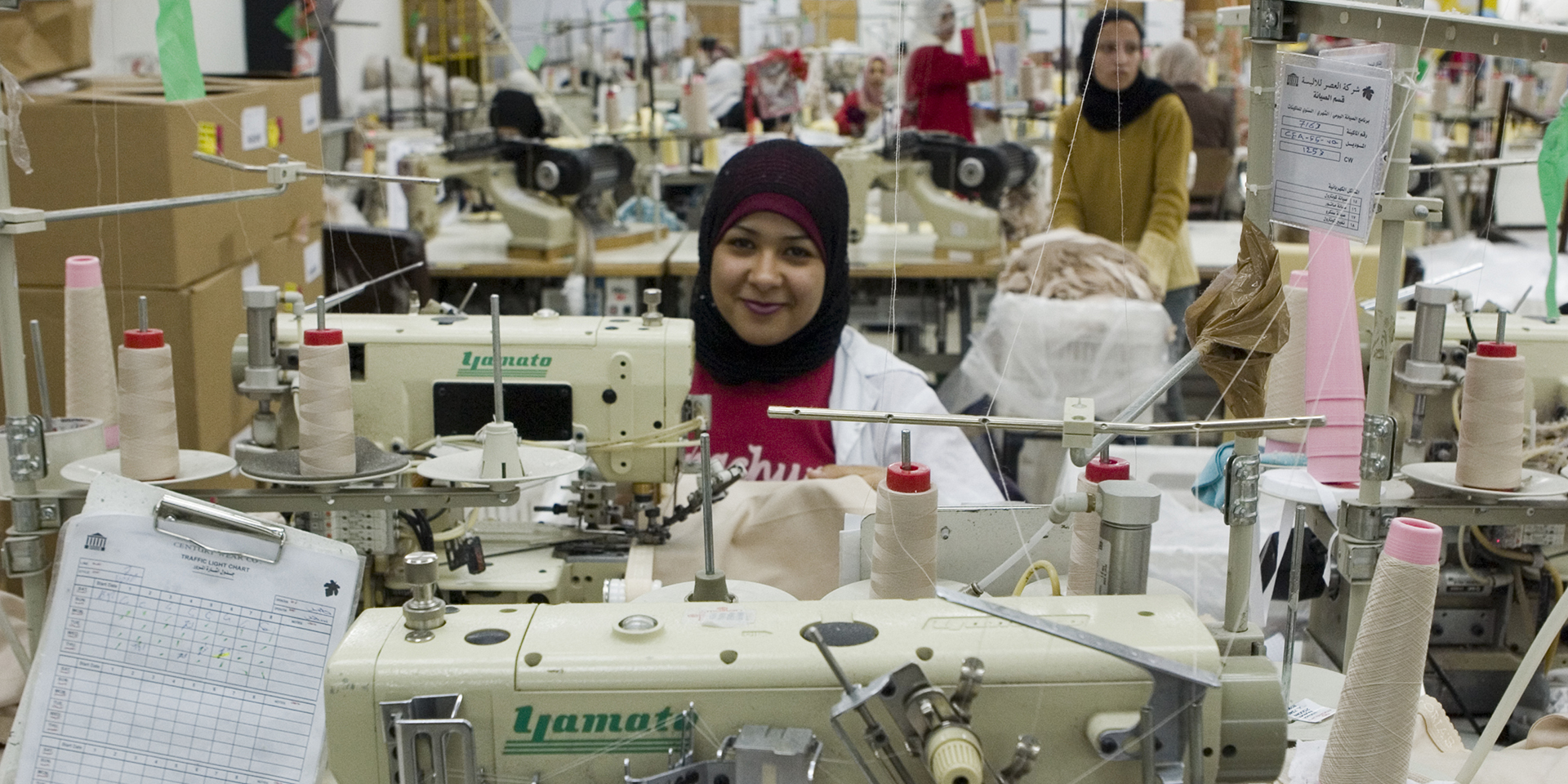 A woman smiles from behind a sewing machine at Century Wear Factory in Irbid, Jordan.