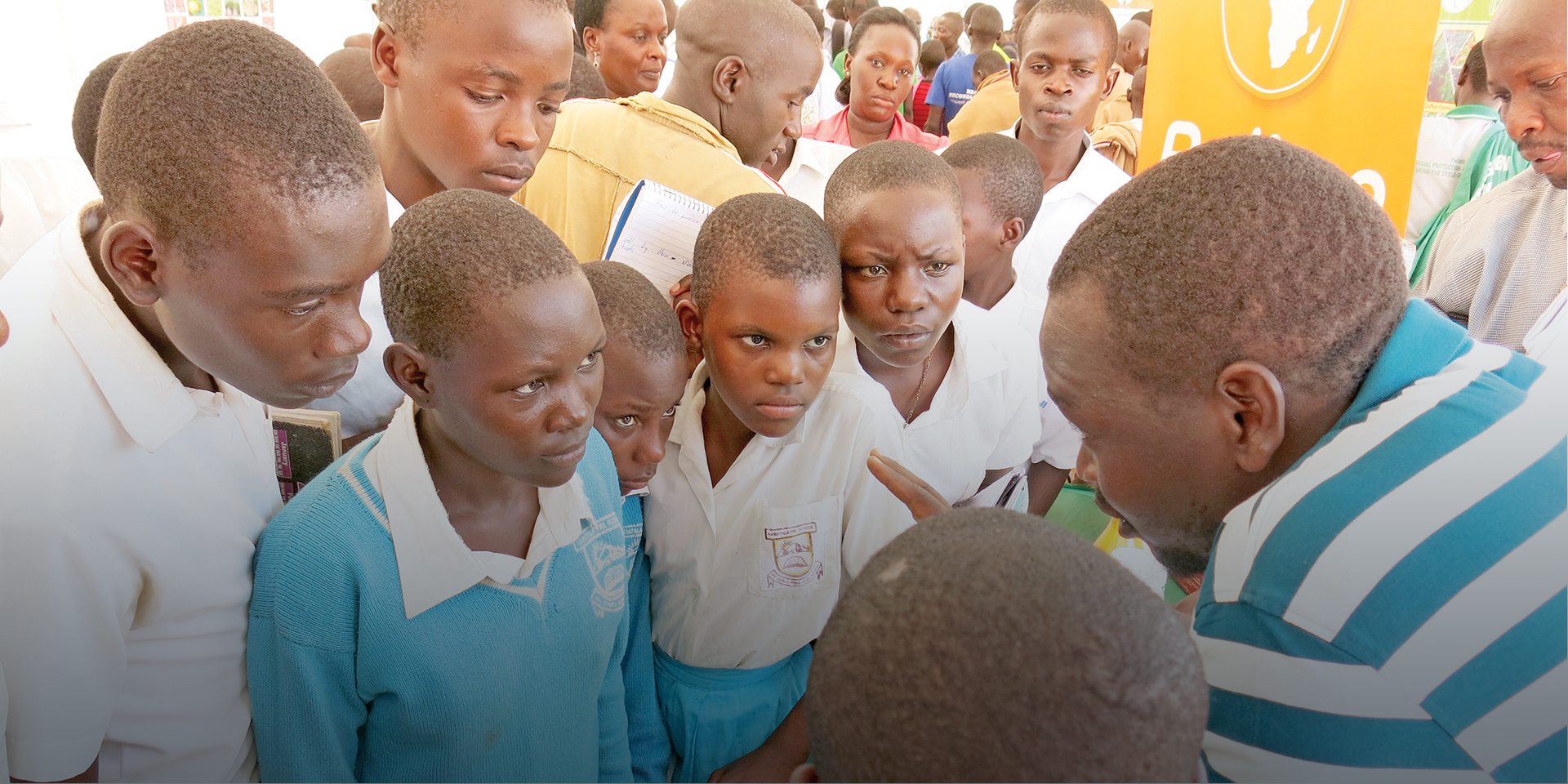 A man speaking to several schoolchildren listening intently.