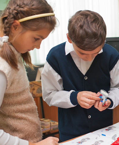 A girl watching as a boy puts together a device while looking at instructions.