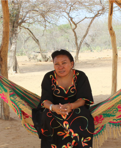 A woman sitting in a hammock in a savanna with a building in the background.