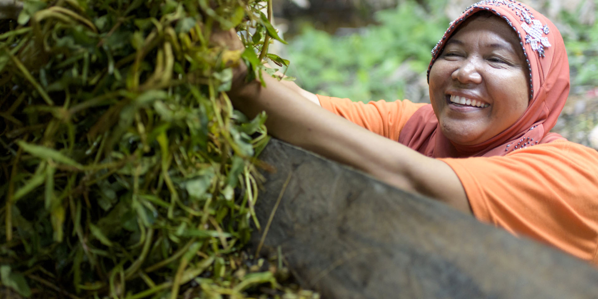 A smiling woman loading greenery into a large container.