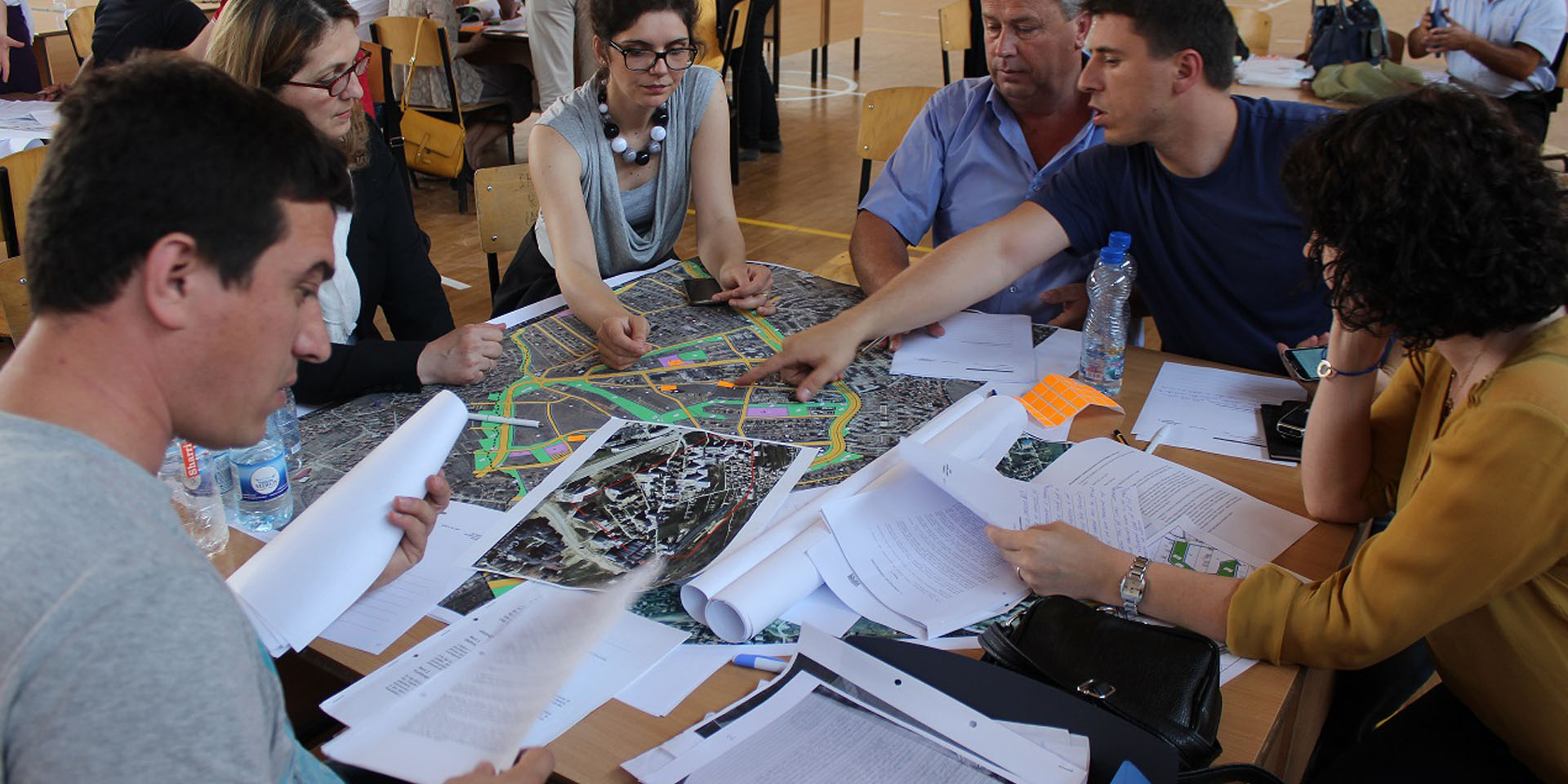 A group of people sitting at a table and discussing a large map laid out between them.