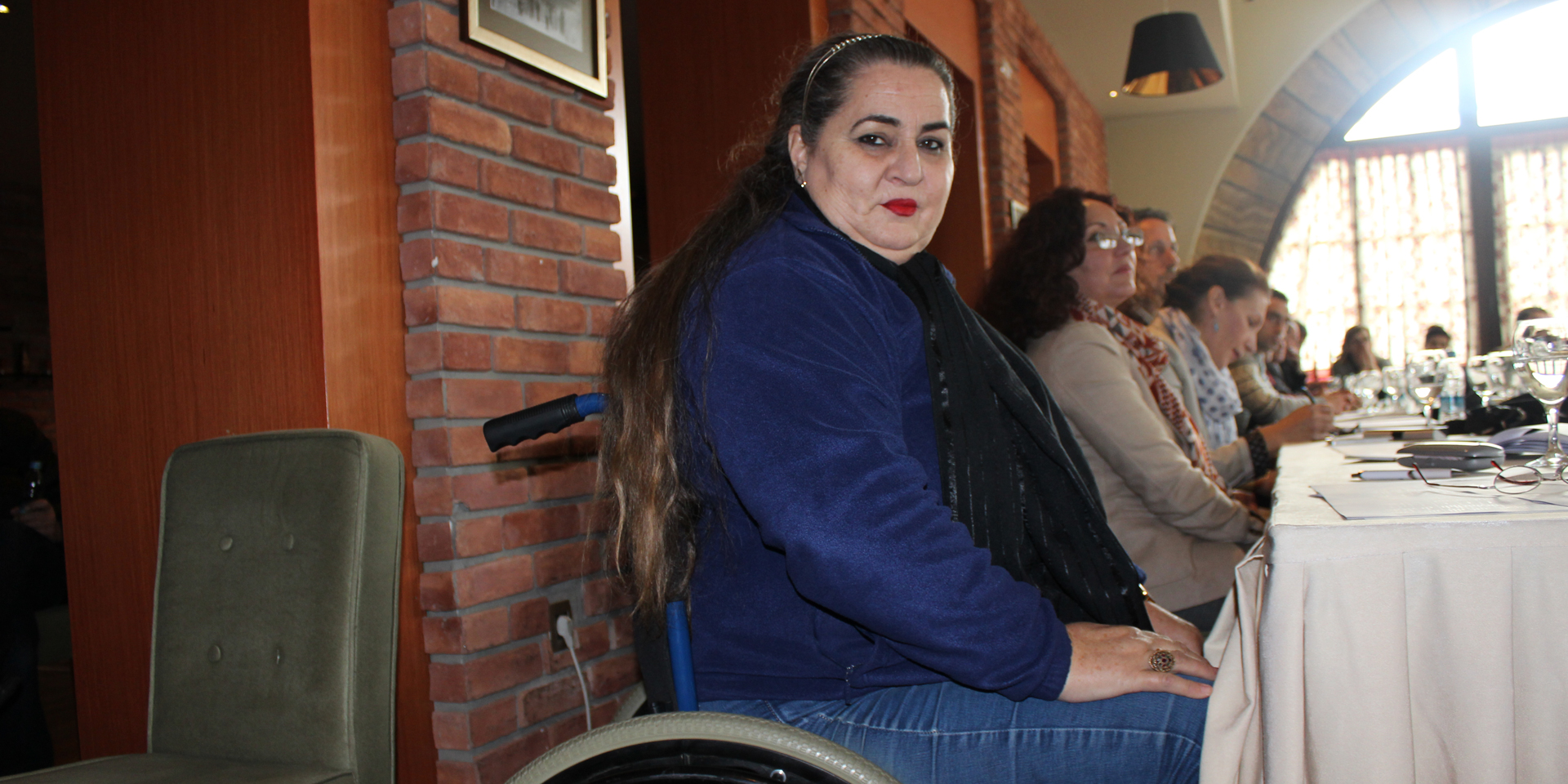 Image of a woman in a wheelchair sitting alongside others at a large table.