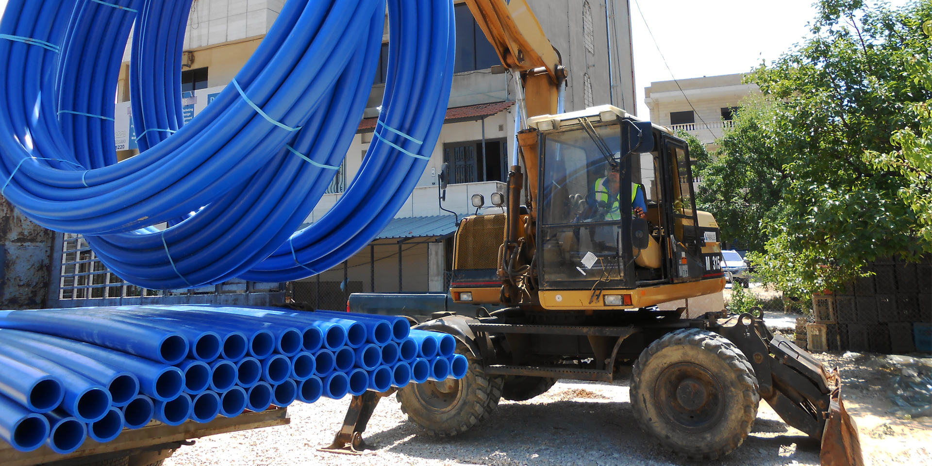 Image of a motorized crane moving large blue pipes onto a pile.