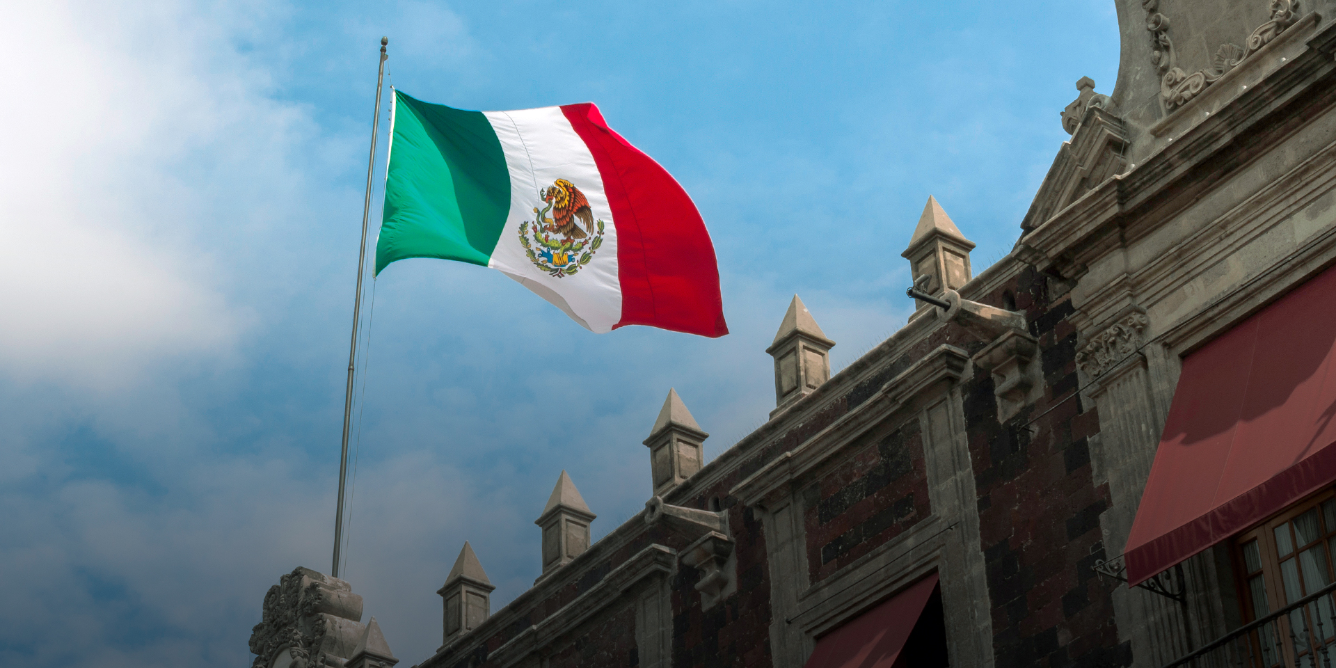 Image of the roof of a building with the Mexican flag on a flagpole waving.