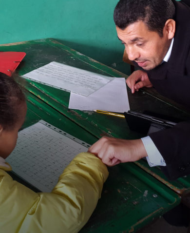 A man sitting at a table across from a child teaching her the alphabet.
