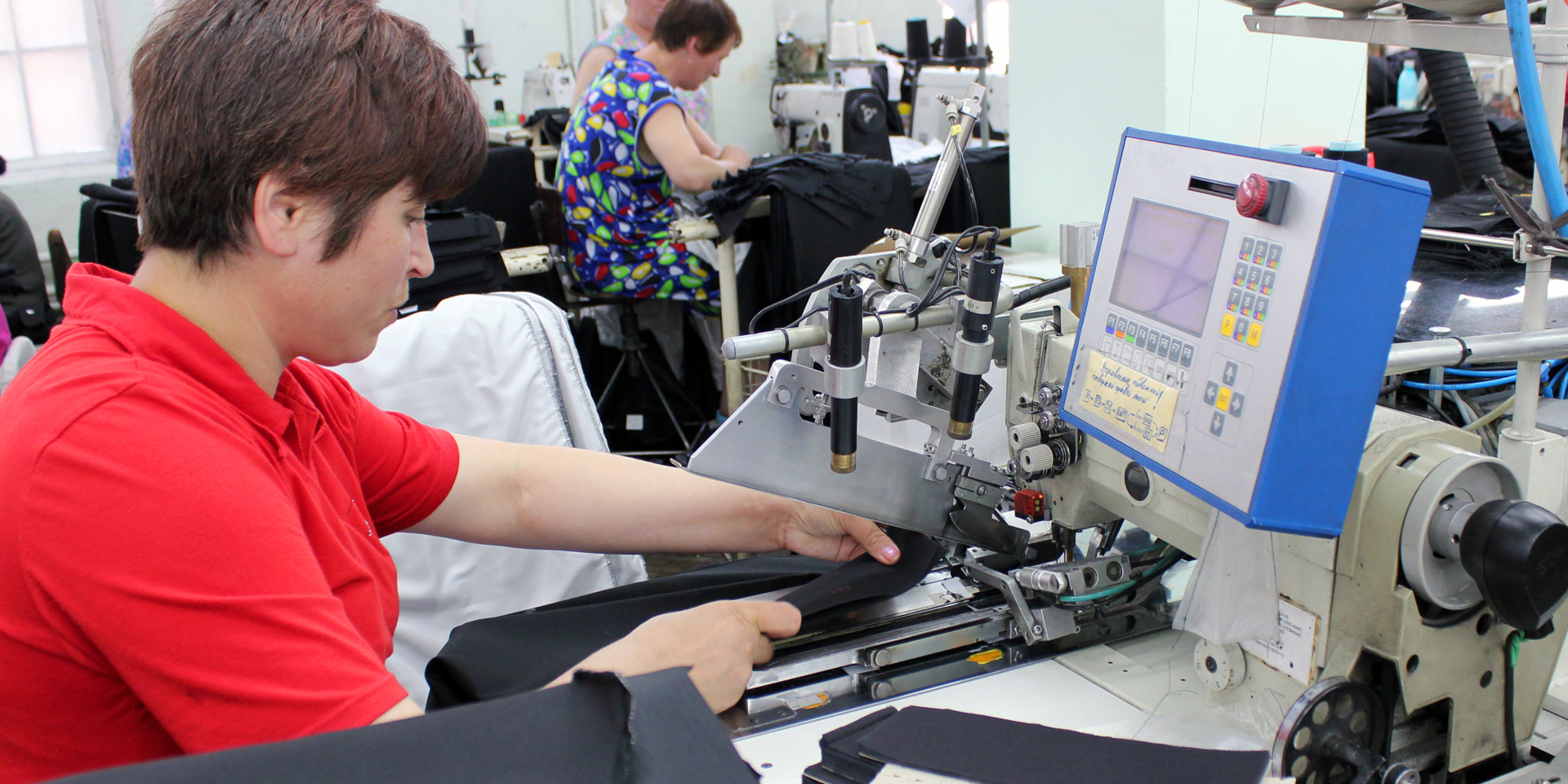A person using an advanced sewing machine with a blue control panel in front of her.