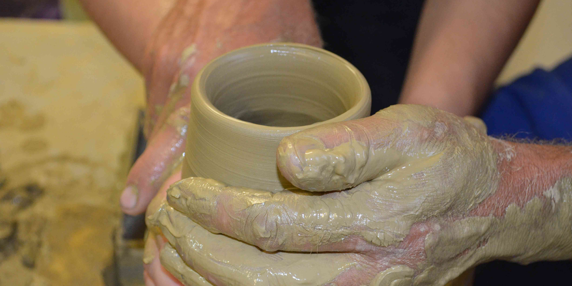A close-up of hands forming pottery on a wheel.