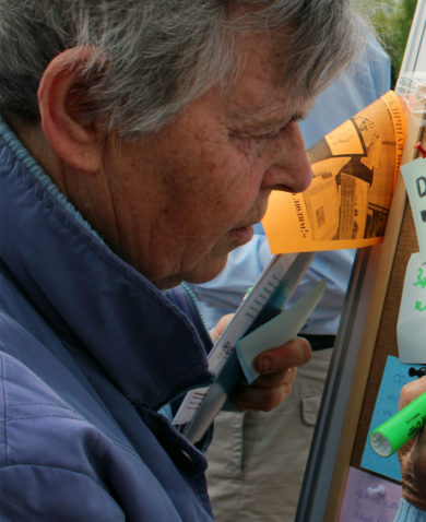 A man outside writing on a sticky note pinned to a corkboard.