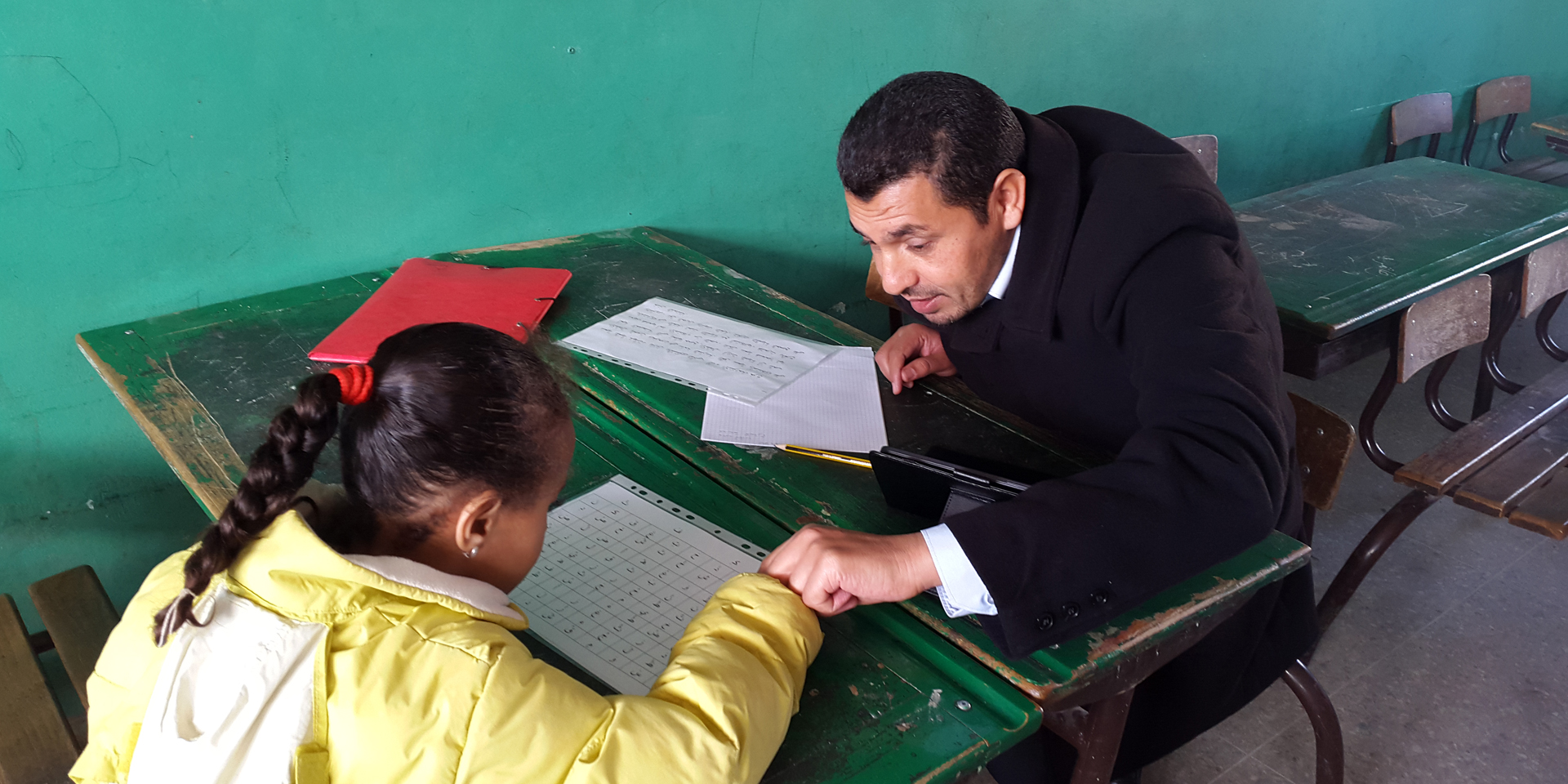 A man sitting at a table across from a child teaching her the alphabet.