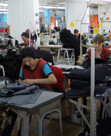 A room filled with people sitting at tables and sewing pants on individual sewing machines.