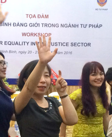 A group of women smiling and giving a presentation in front of a large poster that says "Workshop; Gender Equality in the Justice Sector."