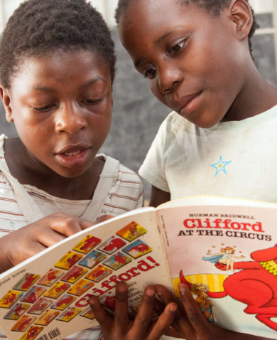 Image of two schoolchildren in a classroom reading a "Clifford" book together.