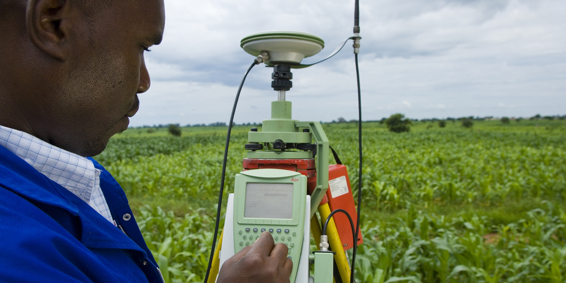 A man surveying farmland with a large green device with a keypad he is using to input figures.