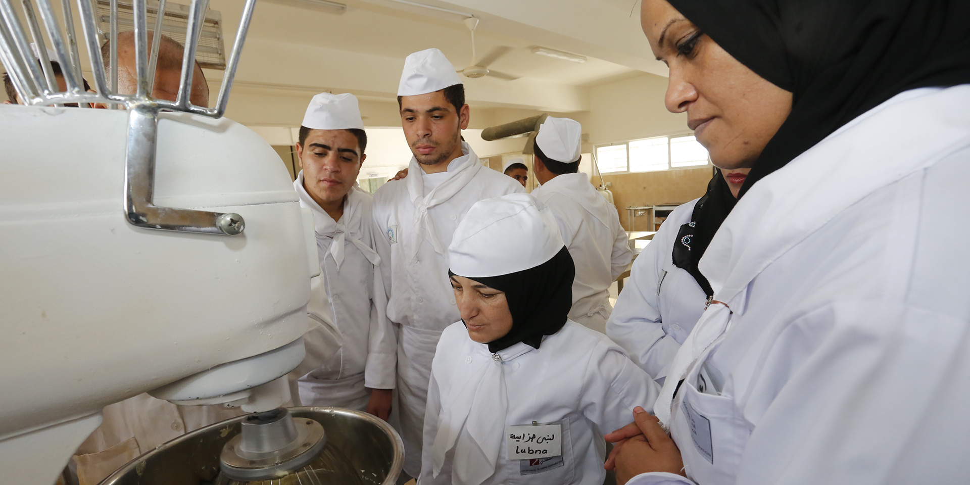 A group of cooks watching someone use a mixing machine.