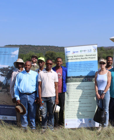 Image of several people in a field posing beside several posters for a training workshop. Behind them is a large drone marked "Skytem."